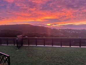 A sunset view from a grassy area with a wooden fence in the foreground.