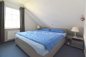 Ein Schlafzimmer mit einem Bett, zwei Nachttischen, einem Fenster mit Vorhängen und einer Wandleuchte.