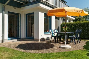 A patio with a table and chairs, an umbrella, and a window with a view of the garden. - Holiday apartment with 2 bedrooms (Prerow)