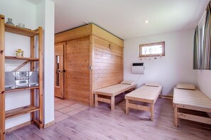 Ein Zimmer mit Holzwänden, einer Holzbank, einem Regal mit elektronischen Geräten und einem Fenster mit Jalousien.