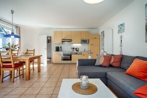 A modern kitchen with wooden cabinets, a microwave, and a dining area with a table and chairs. - Holiday apartment with 2 bedrooms (Prerow)