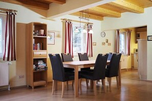 A dining area with a wooden table and chairs, a bookshelf, and a kitchen in the background. - Holiday home in Prerow with swimming pool (Prerow)