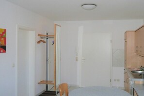 A compact room with a bed, a chair, a small table, a wardrobe, and a kitchenette. - House "Am Brunnen" W.2 (Ostseebad Prerow)