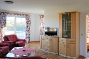 A living room with a sofa, a glass coffee table, a television, and a cabinet with glass doors. - House "Am Brunnen" W.2 (Ostseebad Prerow)