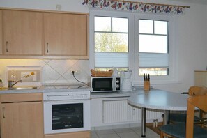 A kitchen with wooden cabinets, a white stove, a microwave, and a window with blinds. - House "Am Brunnen" W.2 (Ostseebad Prerow)
