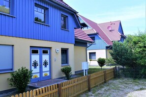 A two-story building with a blue exterior and a red roof, featuring a wooden fence and small trees in front. - Grüne Str. 36 h "Seenadel" (Prerow)