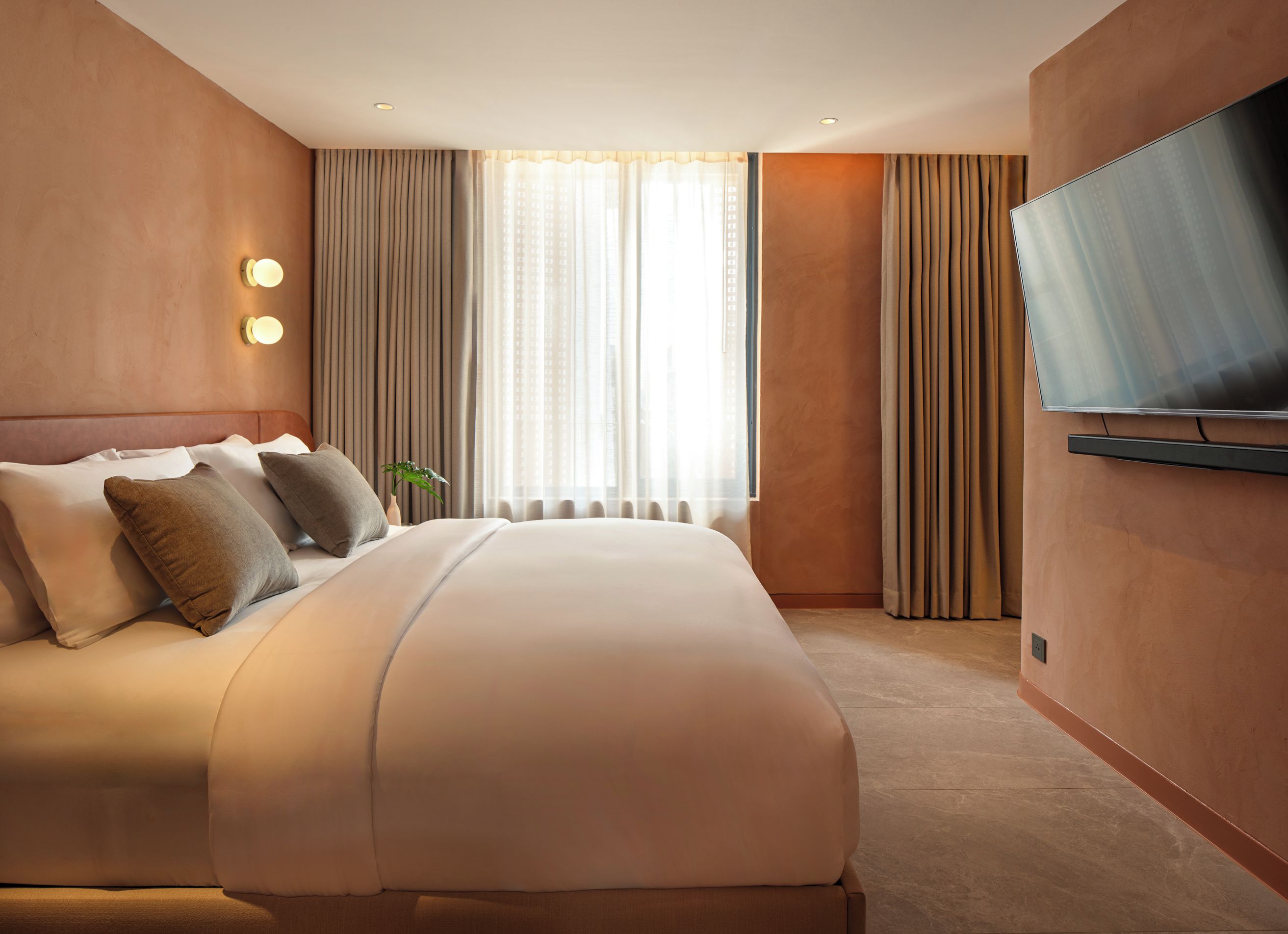 A hotel room with a large bed, a flat-screen TV mounted on the wall, and a window with curtains.