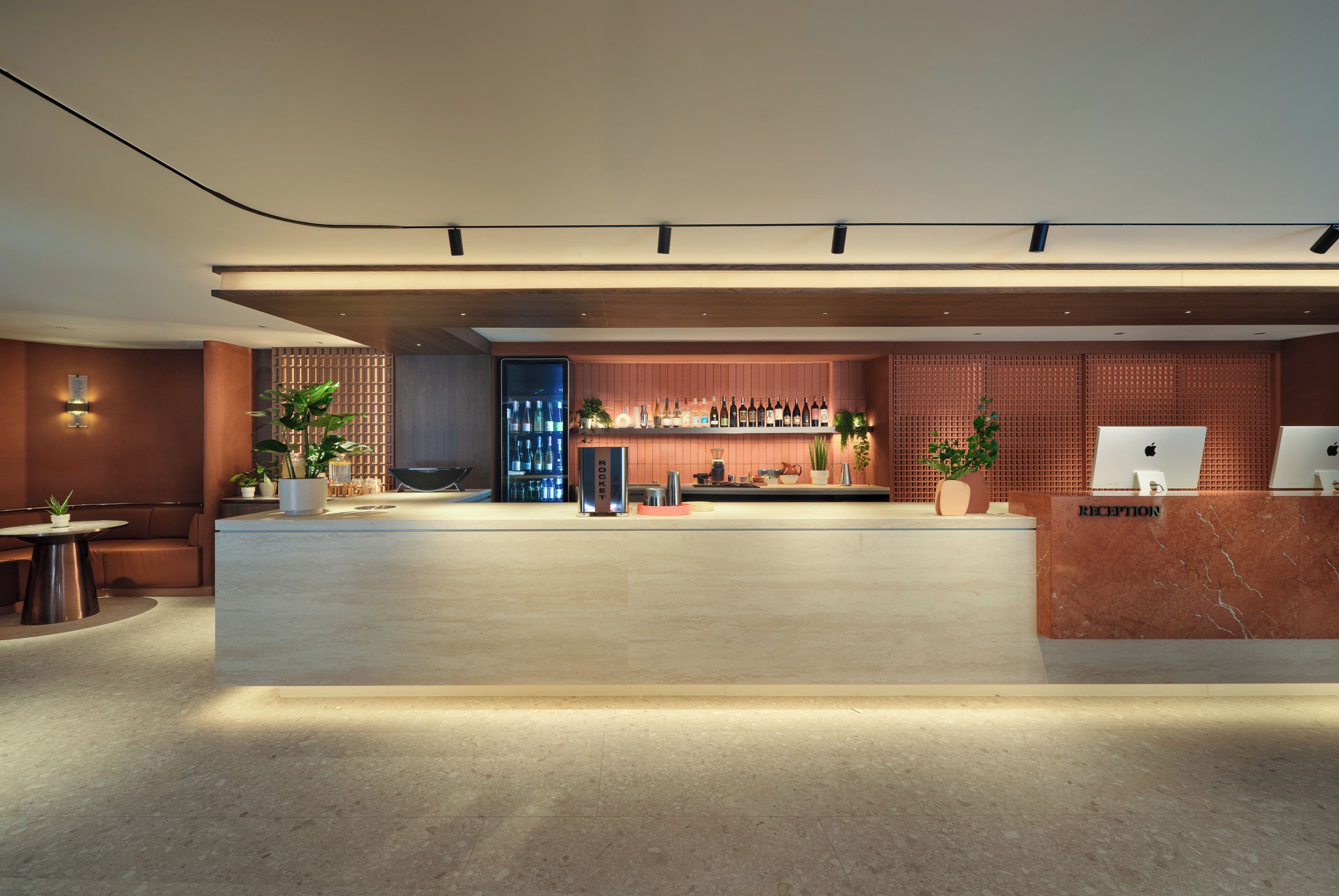 Ein moderner Empfangsbereich mit einer Marmor-Theke, einer Sitzecke mit Sofa und Tisch sowie einer Bar mit Regalen voller Flaschen.
