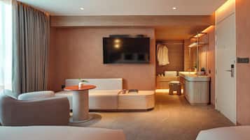 A modern hotel room with a sofa, a small table, a TV, a bathroom with a mirror, and a wardrobe.