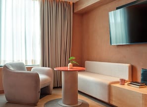 Uma sala de estar moderna com um sofá, duas poltronas, uma mesa de centro redonda, uma televisão de tela plana na parede e um vaso com planta.