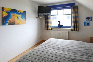 Ein Schlafzimmer mit einem Bett, einem Fenster mit Vorhängen, einem Heizkörper und einem Gemälde an der Wand.