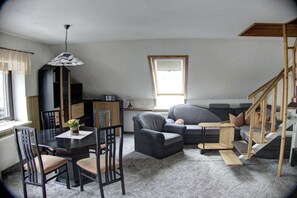 Een woonkamer met een eettafel, stoelen, een bank, een bijzettafeltje en een trap.
