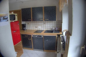 Een kleine keuken met donkere kastjes, een rode koelkast en een magnetron.