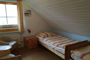 Ein Schlafsaalzimmer mit zwei Einzelbetten, einem Holznachttisch, einem Korbstuhl und einem Fenster mit Jalousien.