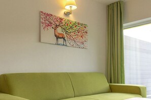 A room with a green sofa, a wall-mounted lamp, and a painting of a deer and tree. - Bungis holiday home directly on the lake, H1 (Joachimsthal)