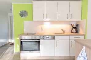 A kitchen with white cabinets, a built-in oven, a coffee maker, and a wall clock. - Bungis holiday home directly on the lake, H1 (Joachimsthal)