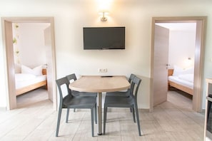 A room with a bed, a TV mounted on the wall, a round table with chairs, and a door leading to another room. - Bungis holiday home directly on the lake, H1 (Joachimsthal)