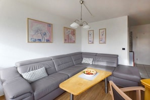 A modern living room with a grey sectional sofa, a wooden coffee table with a bowl of fruit, and framed artwork on the wall. - House "Am Brunnen" W.4 (Ostseebad Prerow)