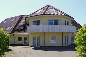 A two-story house with a sloped roof, a balcony on the second floor, and a paved driveway. - House "Am Brunnen" W.4 (Ostseebad Prerow)