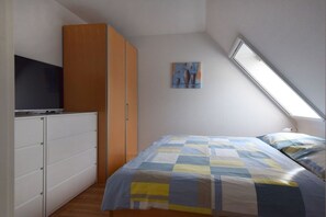 A bedroom with a bed, a wardrobe, a television, and a painting on the wall. - House "Am Brunnen" W.4 (Ostseebad Prerow)