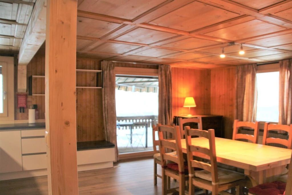 A wooden dining room with a table and chairs, a lamp, and a view through a window.