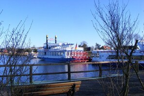 Ein Flussufer mit einem großen Boot, einer hölzernen Bank und kahl stehenden Bäumen.