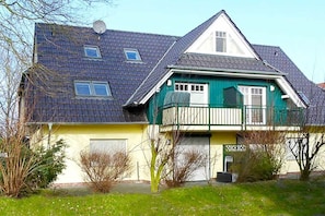A two-story residential building with a sloped roof, a balcony on the upper floor, and a garage door. - Green Street 38 A || Prerow (Prerow)