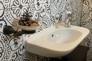 Ein Badezimmer mit einem weißen Waschbecken, einer dekorativen Schale mit Kiefernzapfen und einer Wand mit schwarz-weißen Fliesen.
