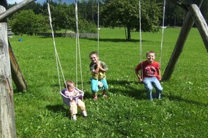A wooden swing set in a grassy area with trees in the background. - Seber-Alpschwendthof family (Mittersill)