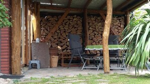 An outdoor patio with a table and chairs, a brick wall, and stacked firewood. - Holiday home with 1 bedroom (Waren \/ Müritz)