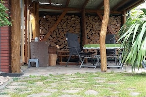 Un patio exterior con mesa y sillas, un muro de ladrillo y leña apilada.