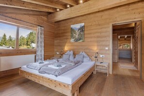 Ein Schlafzimmer einer Holzhütte mit einem Bett, Nachttischen und einem Fenster mit Blick auf Bäume.