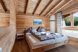 Ein Schlafzimmer einer Holzhütte mit einem Bett, Kissen, einem Nachttisch, einem Fenster mit Vorhängen und einem Bild an der Wand.