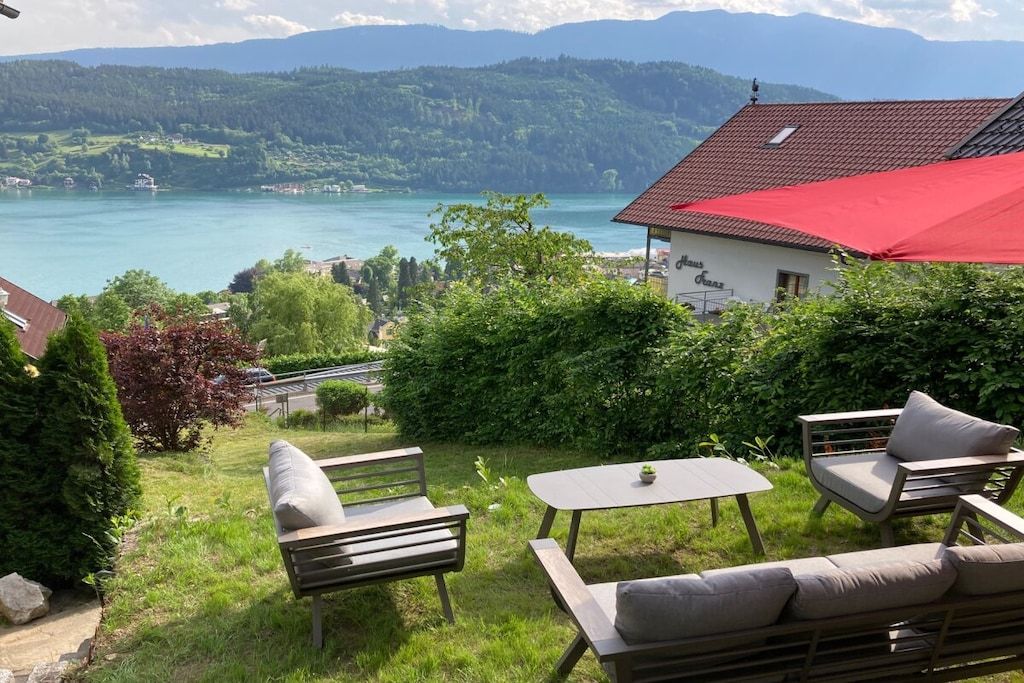 A patio with outdoor furniture, a red awning, and a view of a lake and mountains.