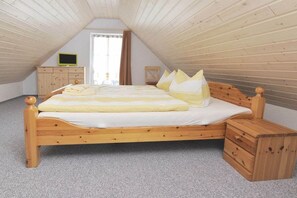 A wooden bed in a room with sloped ceilings, a television on a wooden cabinet, and a window with curtains. - Holiday apartment with 3 bedrooms (Märkische Heide OT Biebersdorf)