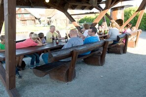 A group of people seated at wooden picnic tables under a covered area with a grill. - Holiday apartment with 3 bedrooms (Märkische Heide OT Biebersdorf)