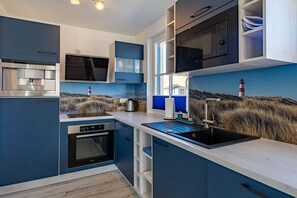 Eine moderne Küche mit integrierten Geräten, einem großen Fenster und Blick auf eine Küstenlandschaft.