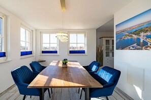 Ein Essbereich mit einem Holztisch, blauen Polsterstühlen und einer Pendelleuchte.