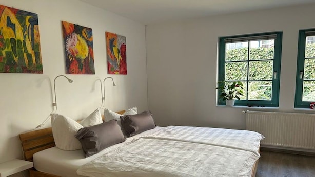 A bedroom with a wooden bed, white bedding, and three colorful paintings on the wall. - Holiday apartment with 2 bedrooms (Waren (Müritz))