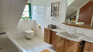 A bathroom with a bathtub, toilet, wooden cabinets, and a sink. - Holiday apartment with 2 bedrooms (Waren (Müritz))