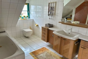 Un baño con bañera, inodoro, armarios de madera y lavamanos.