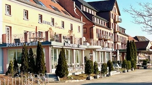 A row of buildings with 'Restaurant Cafe' signs, featuring balconies and a row of potted trees. - Holiday apartment with 2 bedrooms (Waren (Müritz))