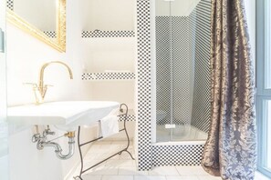 Un baño con lavamanos blanco, grifo dorado y ducha con diseño a cuadros.