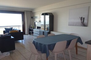 Un comedor moderno con una mesa y sillas, una cocina con armarios, y vista al mar a través de un ventanal.