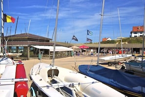 A marina with multiple boats docked, a building with a sloped roof, and flags. - Holiday apartment with 2 bedrooms (Koksijde)