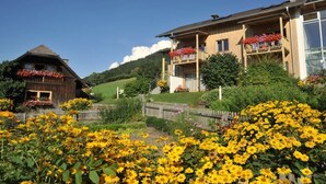 Une maison en bois avec un balcon et un jardin où poussent des tournesols.