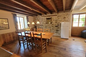 A rustic kitchen with a wooden table, chairs, a stone wall, and a white refrigerator. - Authentic gîte with terrace and shared pool (Saint-Saud-Lacoussière)