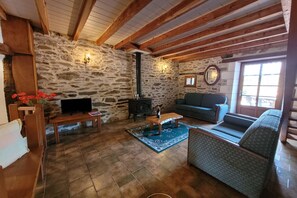A cozy living room with a stone wall, a fireplace, a sofa, and a television. - Charming and spacious gîte with shared pool (Saint-Saud-Lacoussière)