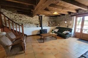 Ein gemütliches Wohnzimmer mit einer Steinwand, einer Holztreppe, einem schwarzen Herd, einem Ledersofa und einem Couchtisch.