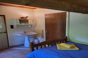 Une chambre à coucher avec un lit en bois, une couvre-lit bleue, un lavabo blanc et une porte en bois.